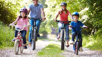 Uma família de quatro pessoas em bicicletas numa trilha de cascalho, rodeada por vegetação.