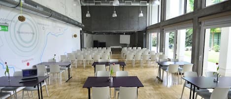 A conference room with white chairs, tables, and a large screen.