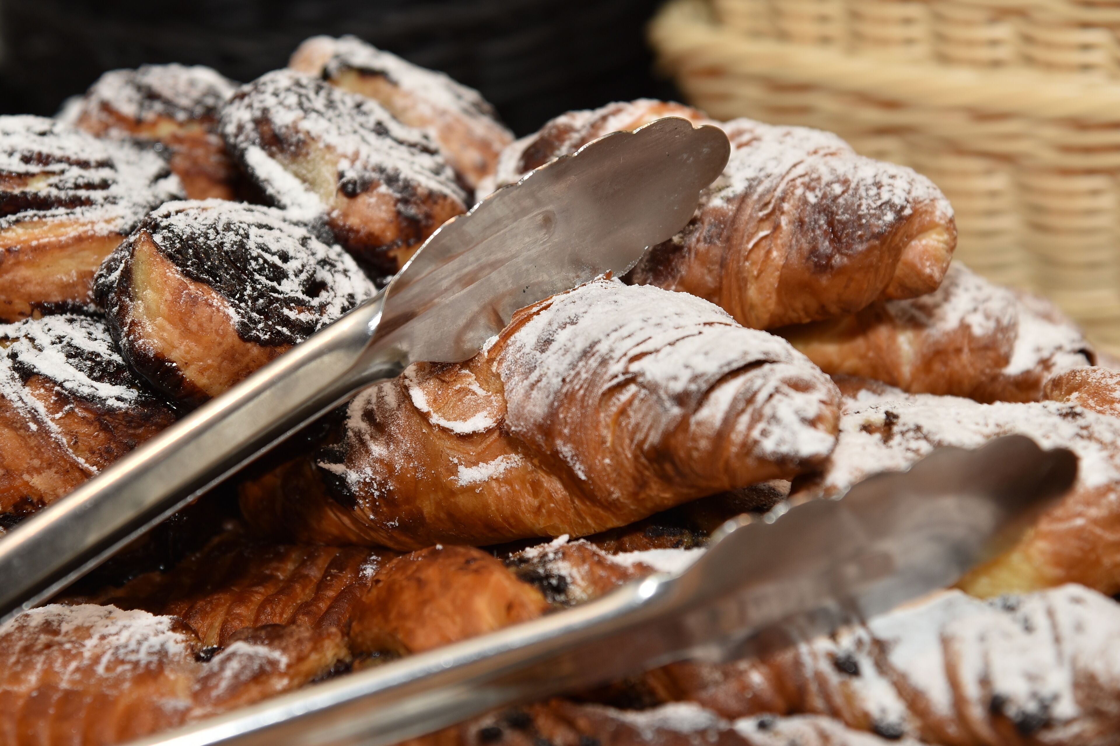 Eine Auswahl an Gebäck auf einer Tablett, darunter Croissants und Schokoladenguss, bestäubt mit Puderzucker.