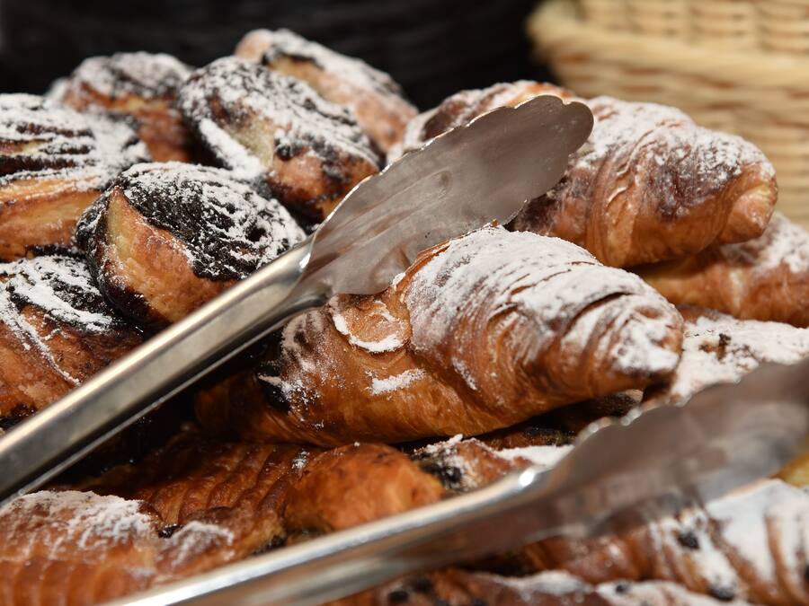 A tray of assorted pastries, including croissants and chocolate-covered items, dusted with powdered sugar.