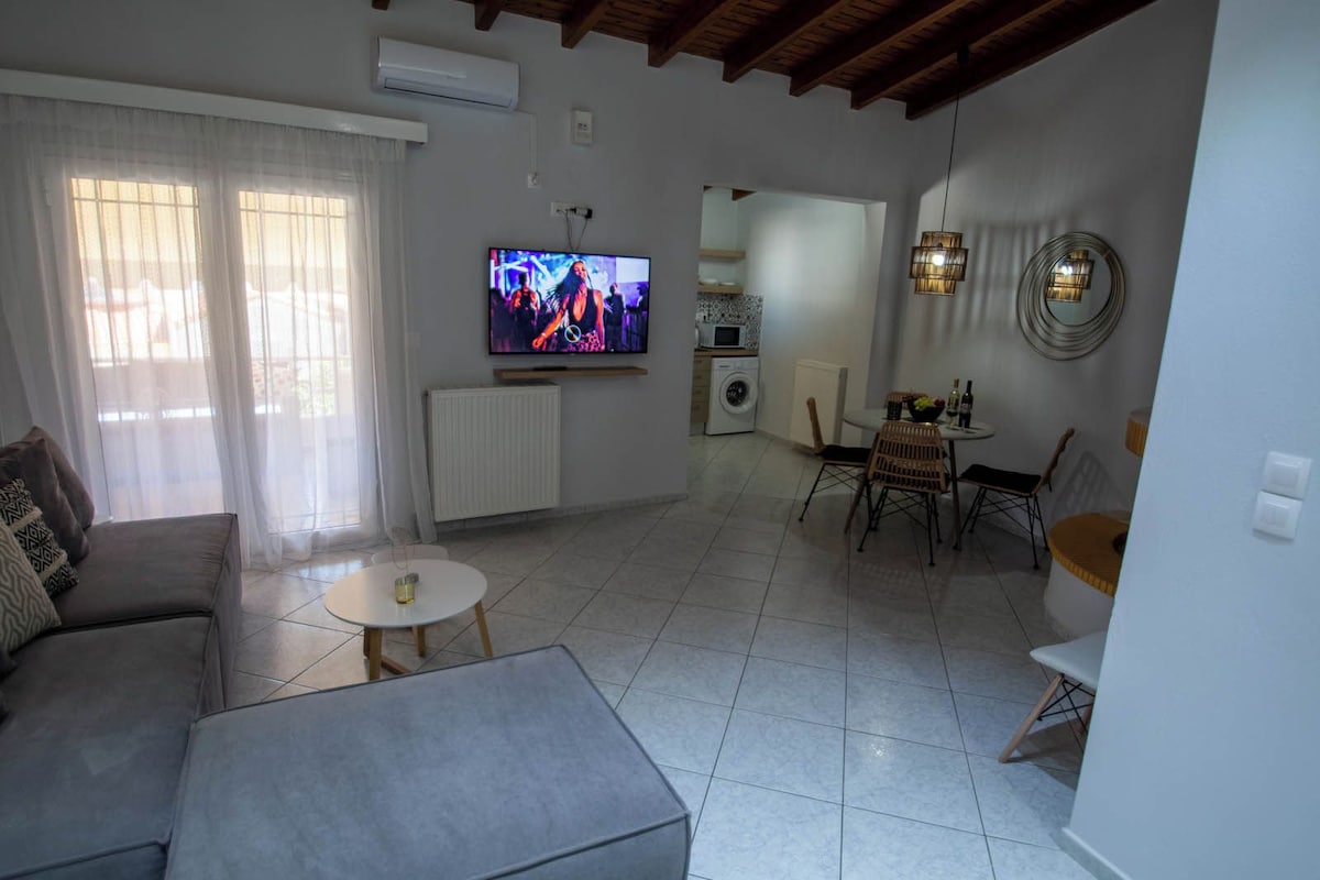 Uma sala de estar com sofá, mesa de centro, televisão e um espaço de jantar com cadeiras e mesa.