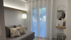 A modern living room with a grey sofa, a wooden coffee table with two glasses, a small stool, and a mirror on the wall. - Avres Apartments (Skiathos)