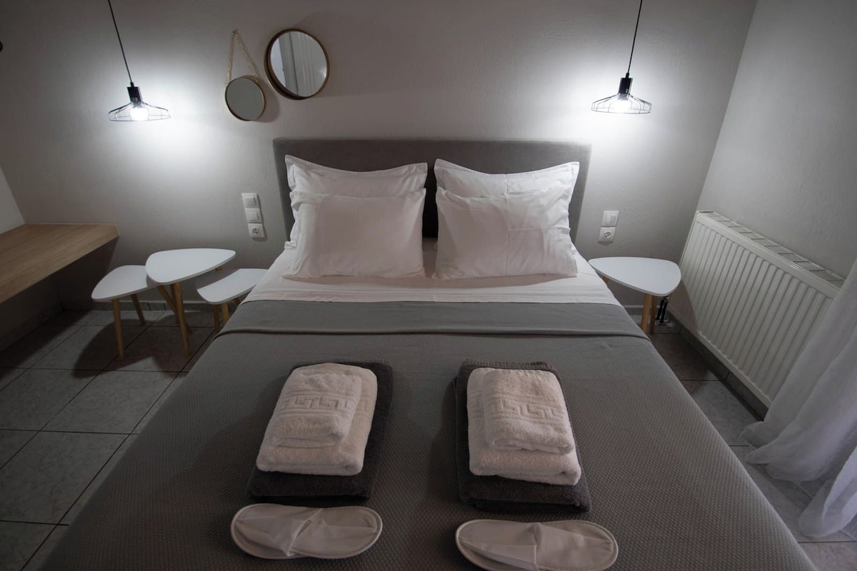 A neatly made bed with two pillows, a bedside table, a small round table, and a bench.