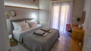 A bedroom with a bed, bedside tables, a chair, a desk, and a window with curtains. - Avres Apartments (Skiathos)