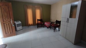 Una habitación con piso de baldosas, puerta de madera, aire acondicionado blanco, una mesa con sillas y un armario.