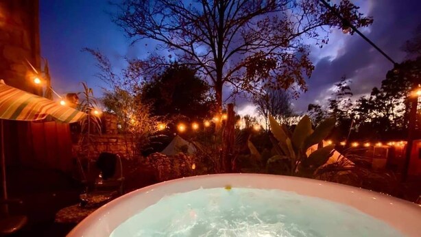 Un jacuzzi en un entorno exterior con luces colgantes y árboles al fondo.