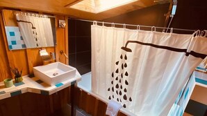 Un baño con techo de madera, un lavamanos blanco, una bañera con cortina de ducha y un espejo.