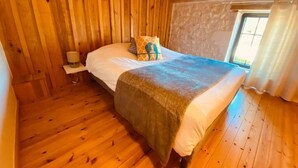 Una habitación con paneles de madera, una cama, una mesita de noche y una ventana con cortinas.