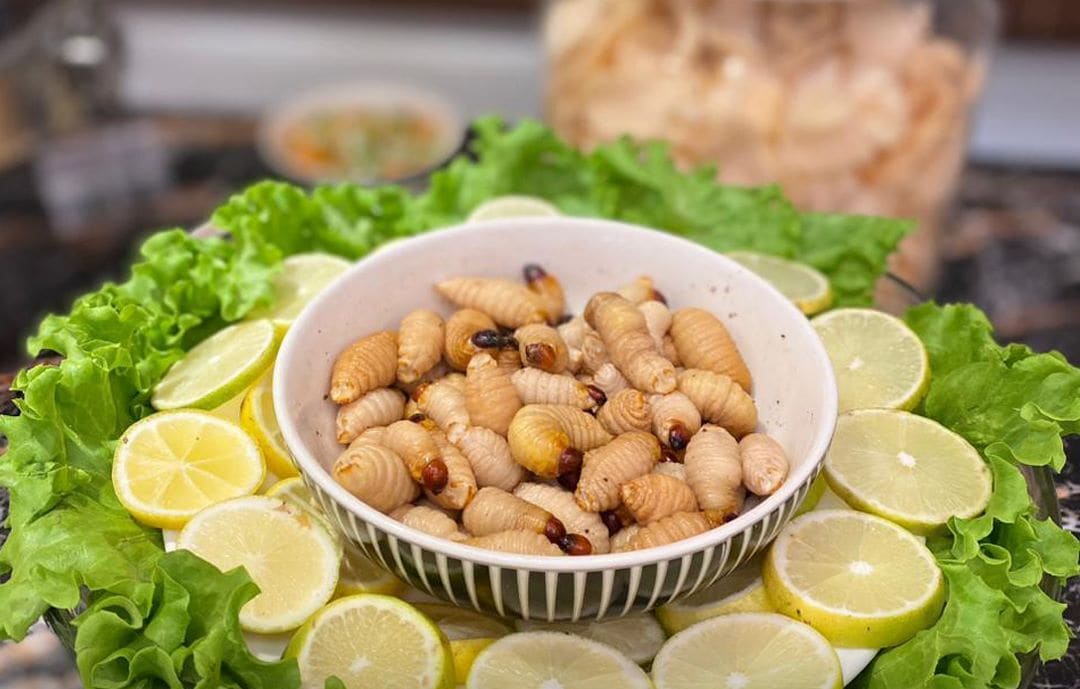 A bowl of fried insects surrounded by lettuce and lime slices.