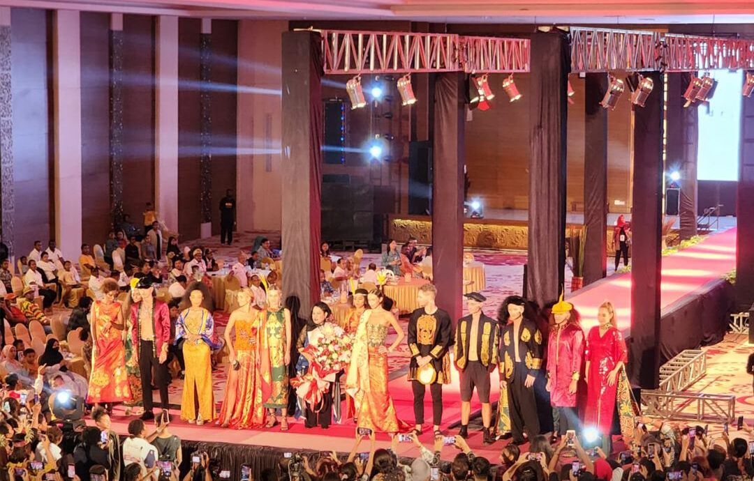 A formal event with attendees on a stage, large columns, and a crowd of spectators.