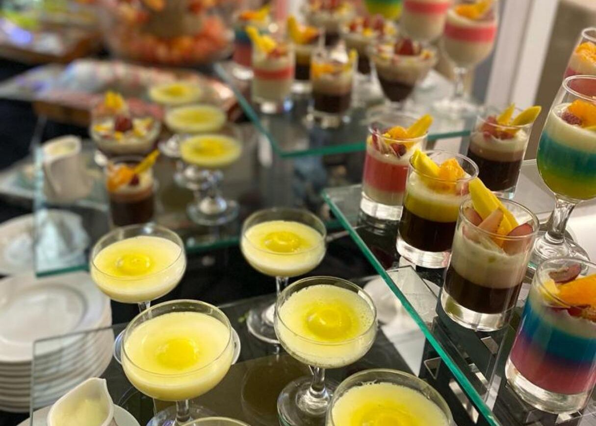 Diversos postres y bebidas dispuestas sobre una mesa de vidrio, probablemente en un bufé o evento.