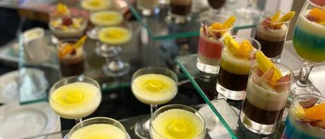 Diversos postres y bebidas dispuestas sobre una mesa de vidrio, probablemente en un bufé o evento.