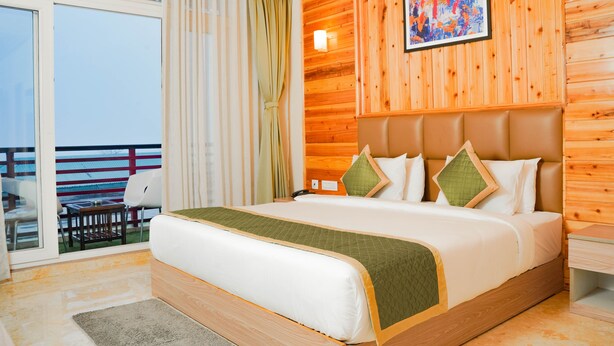 Een hotelkamer met een groot bed, houten paneelwanden, een balkon met uitzicht en een schilderij aan de muur.