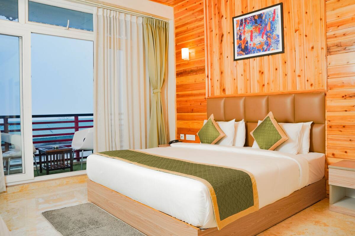 A hotel room with a large bed, wooden panel walls, a balcony with a view, and a painting on the wall.