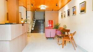 Een hotel receptie met een receptiebalie, een trap naar de bovenverdieping en een zithoek met stoelen en een bank.