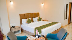 Een hotelkamer met een bed, twee stoelen, een klein tafeltje, een nachtkastje en een spiegel.