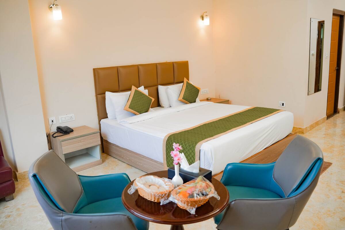 A hotel room with a bed, two chairs, a small table, a nightstand, and a mirror.