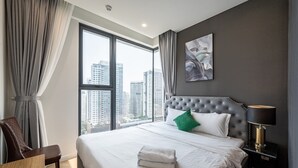 A hotel room with a large window, a bed with white linens, a green pillow, and a grey headboard. - Lumiere Riverside Luxury Apartment (Ho Chi Minh City)
