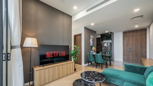 A modern living room with a flat-screen TV, a sofa, a coffee table, and a dining area with chairs and a table. - Lumiere Riverside Luxury Apartment (Ho Chi Minh City)