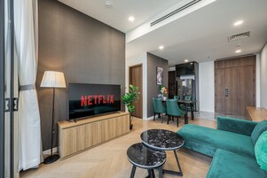 A modern living room with a flat-screen TV, a sofa, a coffee table, and a dining area with chairs and a table.