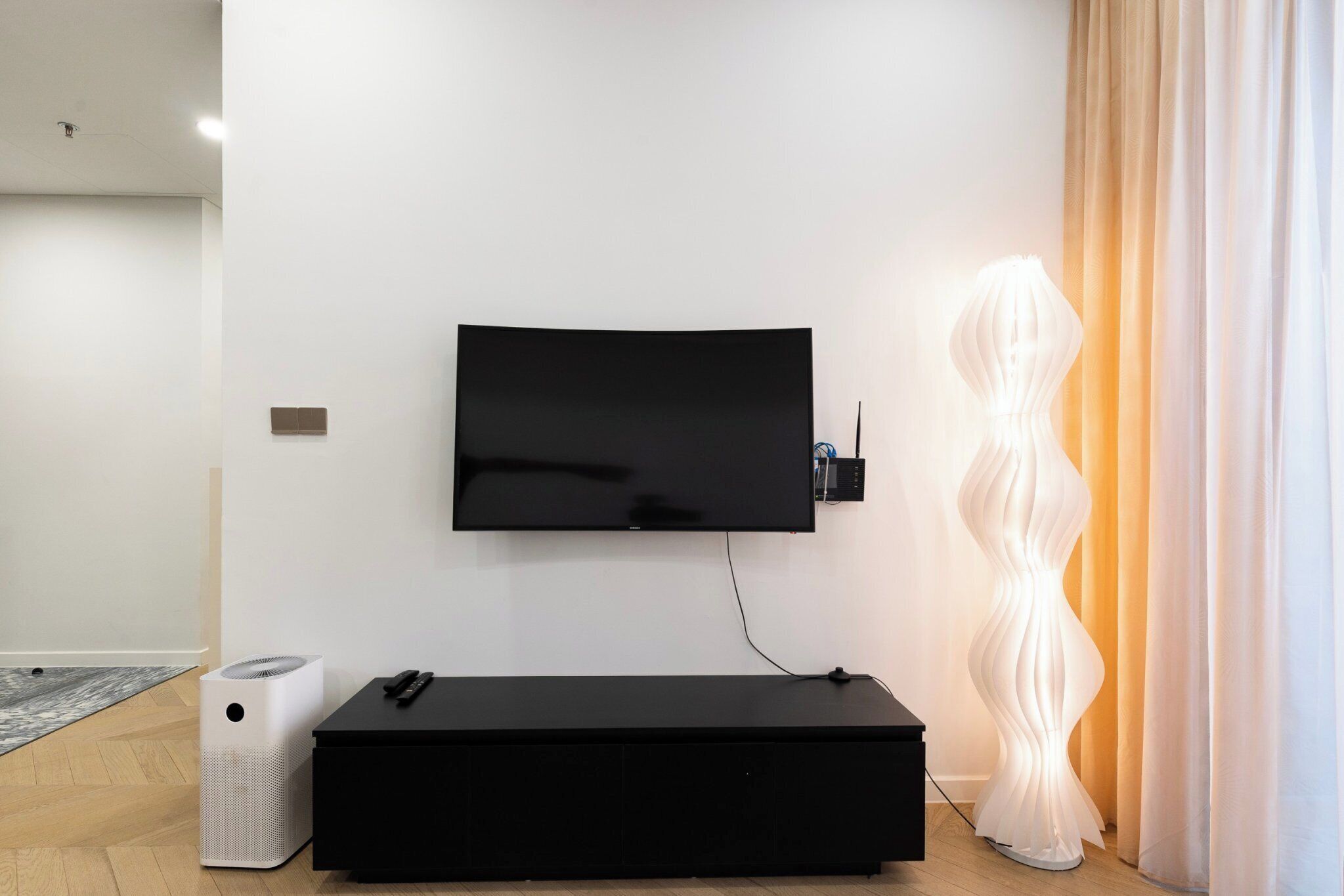 A modern living room with a flat-screen TV mounted on the wall, a black entertainment unit, a white speaker, and a decorative white sculpture.
