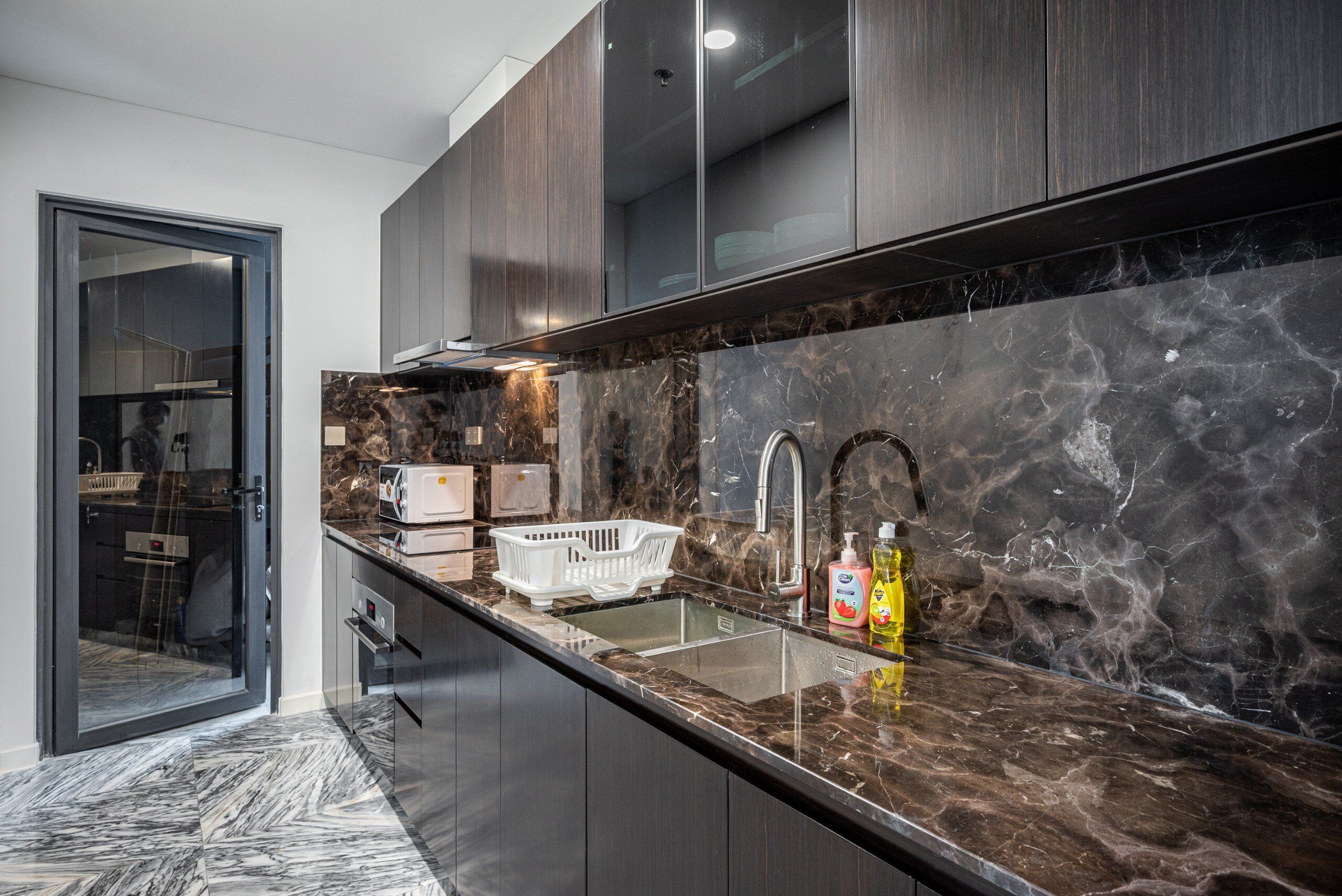 A modern kitchen with dark wood cabinets, a marble countertop, and a built-in sink.