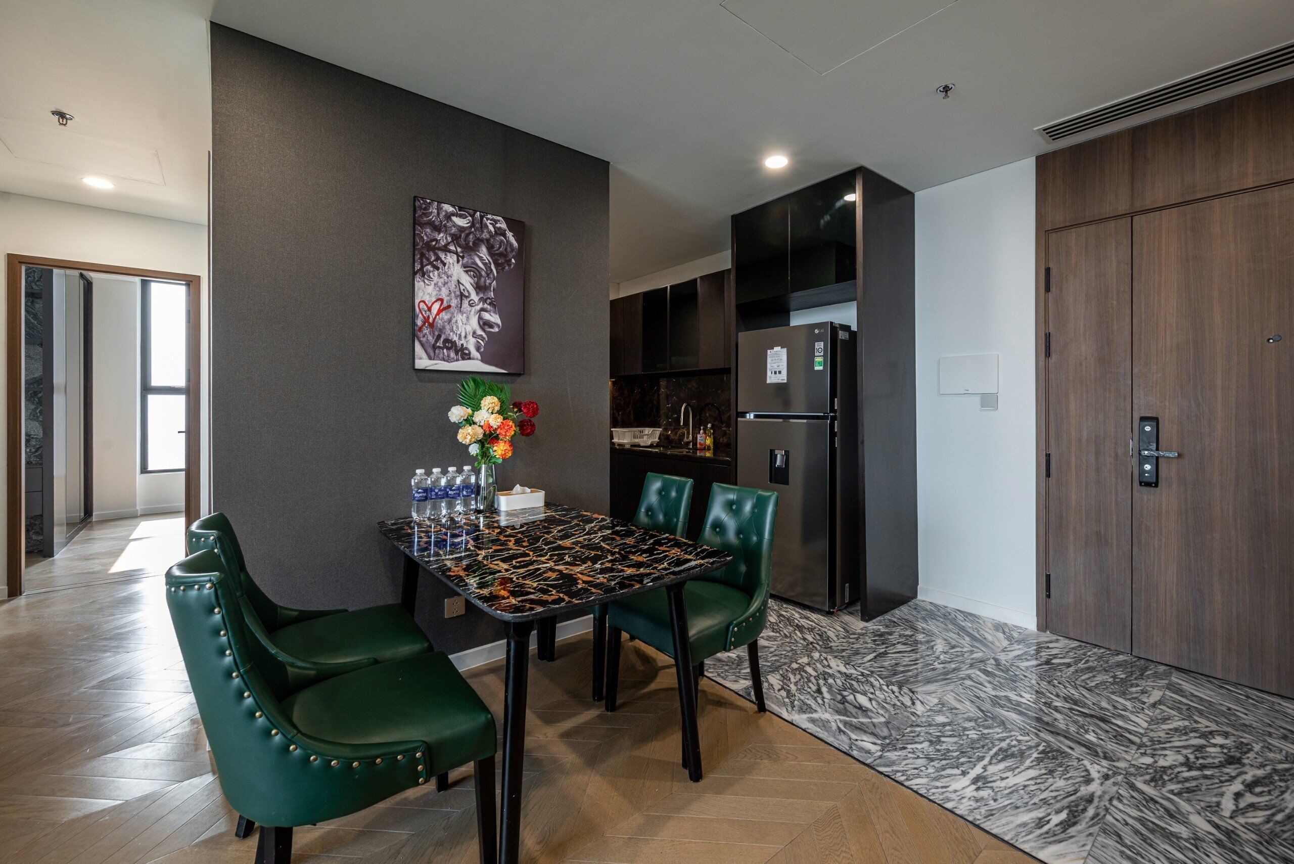 A modern dining area with a marble table, green upholstered chairs, and a decorative vase.