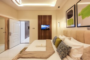 A modern hotel room with a large bed, a flat-screen TV mounted on the wall, and a wooden panel design.