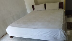 Una cama bien hecha con ropa blanca en una habitación de paredes lisas y suelo de baldosas.
