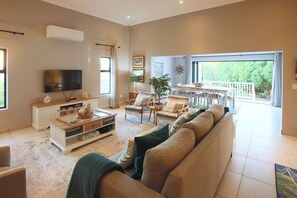 A spacious living room with a large sofa, a TV, and a dining area with a balcony. - Kamen House, Langebaan, 4-Sleeper (Langebaan)
