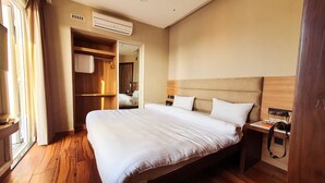 A hotel room with a large bed, wooden flooring, a wardrobe, and a bedside table with a lamp.