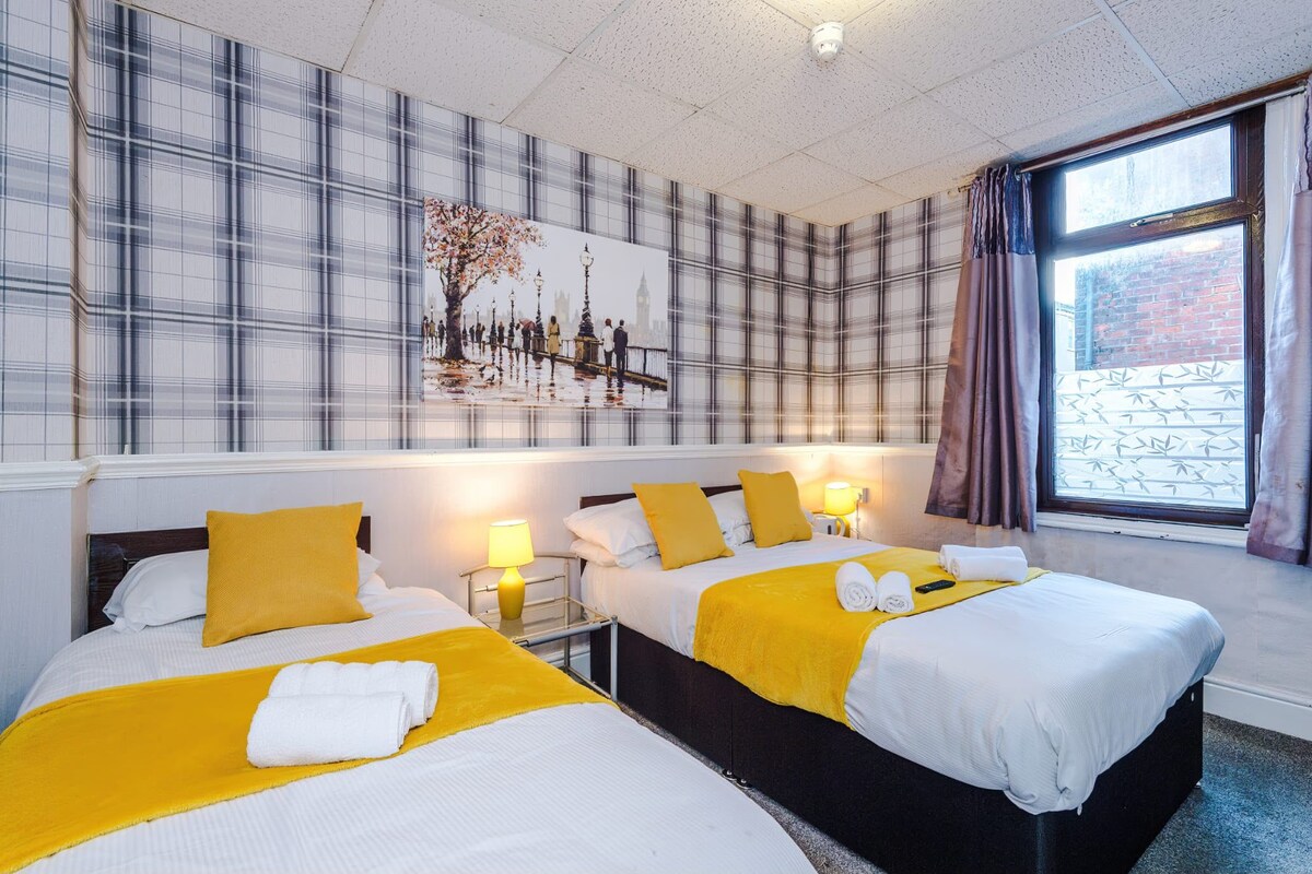 A hotel room with two beds, a large window, and a cityscape view.
