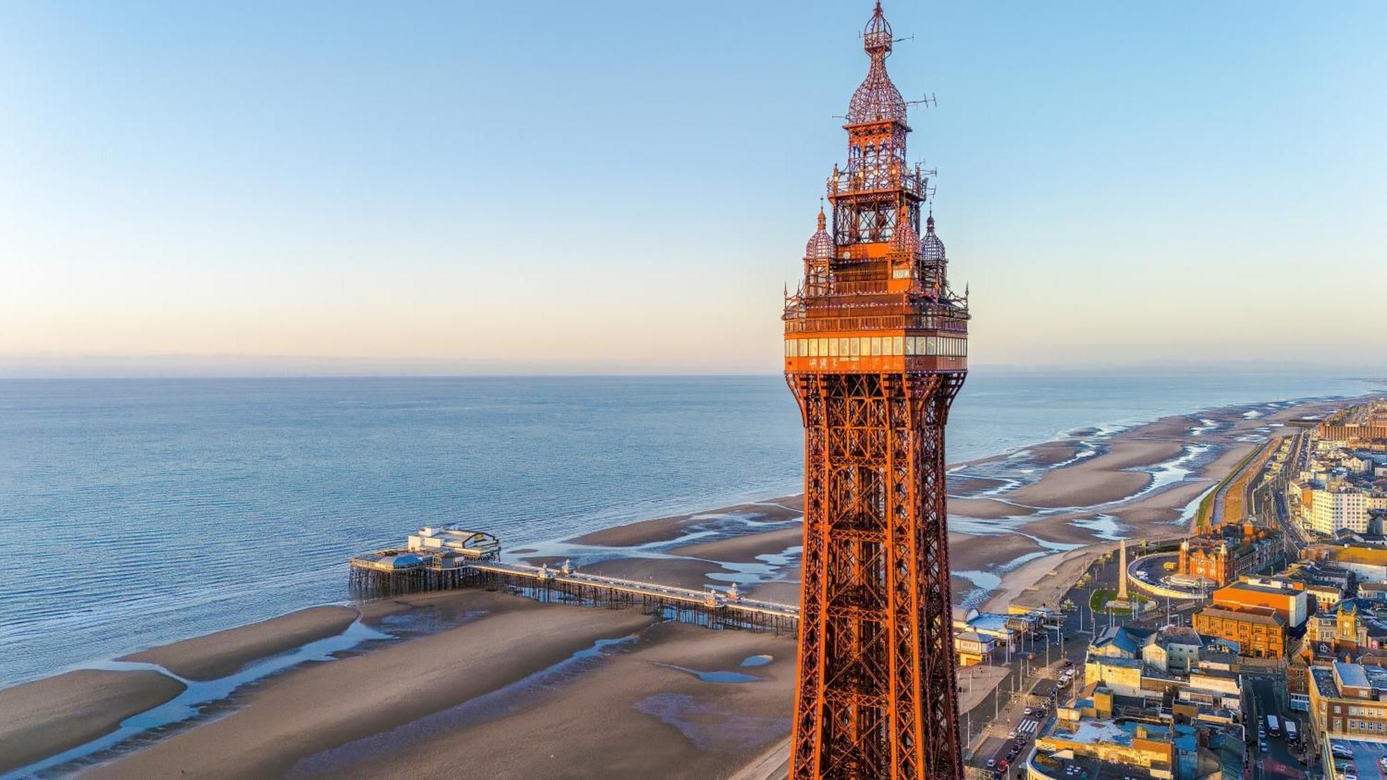 A coastal cityscape with a prominent tower structure, a pier extending into the sea, and a beach area.