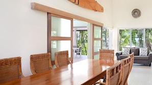 Un coin repas avec une table en bois et des chaises en osier, de grandes fenêtres et une vue sur la verdure environnante.