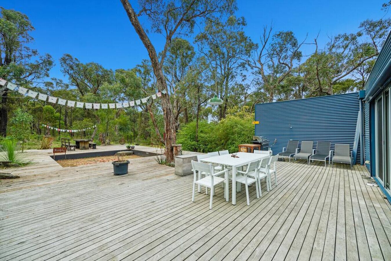 Une terrasse extérieure avec une table et des chaises, entourée de verdure et d’arbres.
