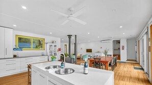 A modern kitchen with a central island, built-in appliances, and a dining area with a wooden table and chairs. - Aireys Bush Retreat - Spacious home with huge deck (Aireys Inlet)