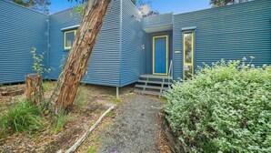 A modern, blue, single-story building with a small porch and a door with a yellow frame. - Aireys Bush Retreat - Spacious home with huge deck (Aireys Inlet)