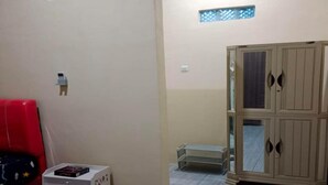 A room with a red couch, a white side table with a book, a beige wardrobe, and a small white cabinet. - Hotel O Ayna Kost Syariah (Singaraja)