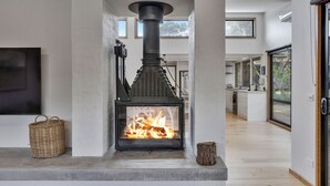Una sala de estar moderna con una estufa de leña, un televisor de pantalla plana grande y vistas al exterior a través de un ventanal.