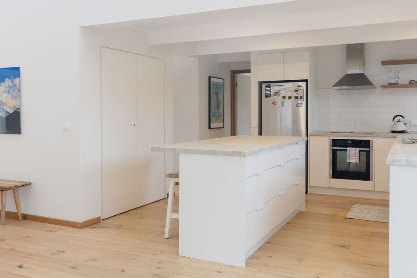 Une cuisine moderne avec des meubles blancs, un îlot central doté de tiroirs, un four encastré et un réfrigérateur en acier inoxydable.