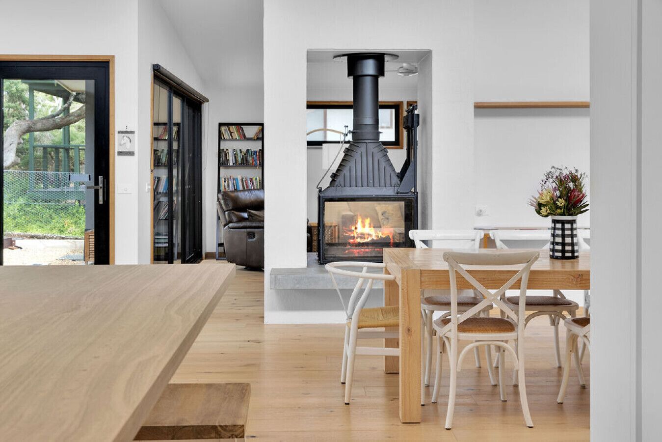 Une cuisine moderne avec un poêle à bois, un coin repas avec des chaises blanches et une bibliothèque remplie de livres.