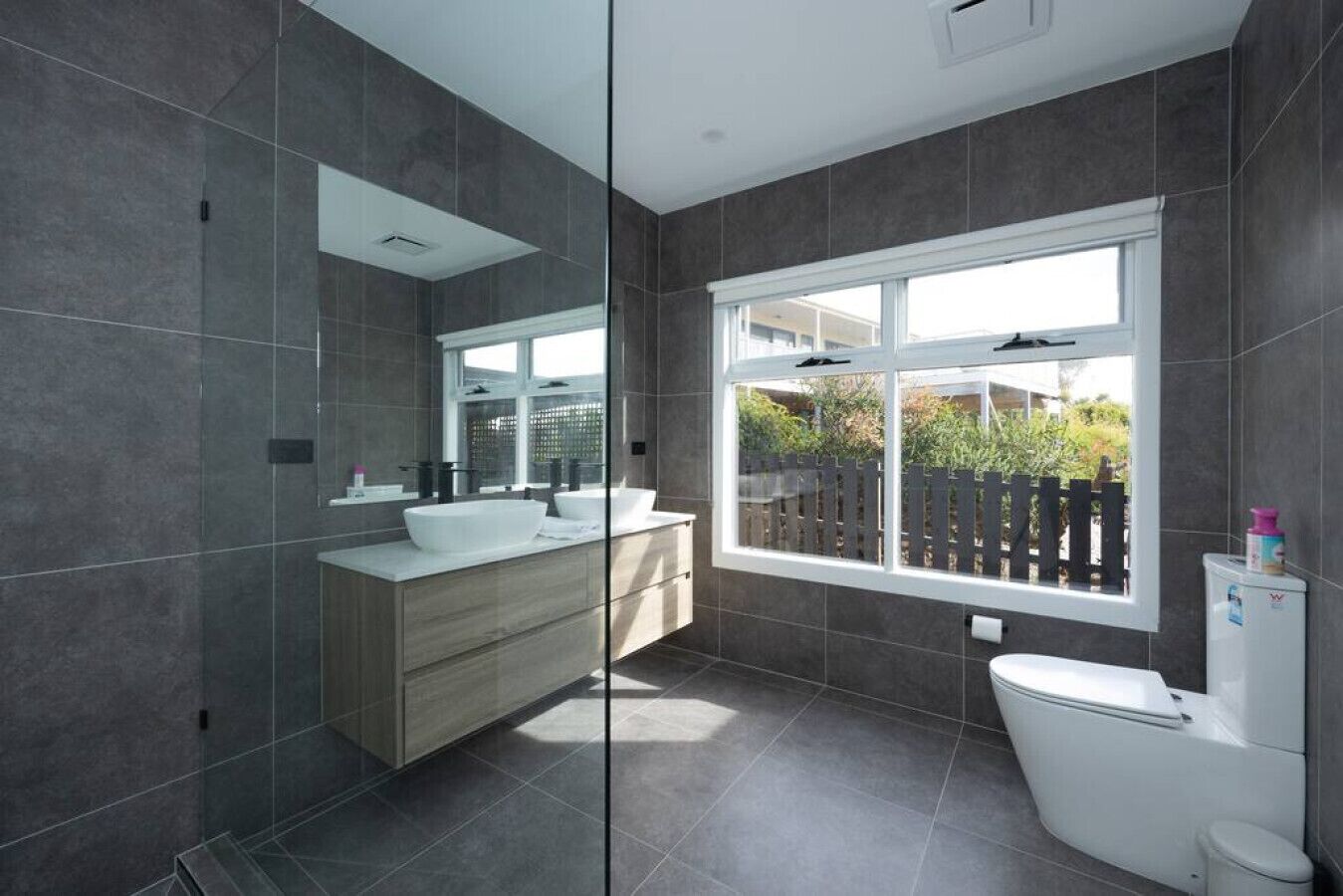 Een moderne badkamer met een groot raam, een inloopdouche en een toilet.