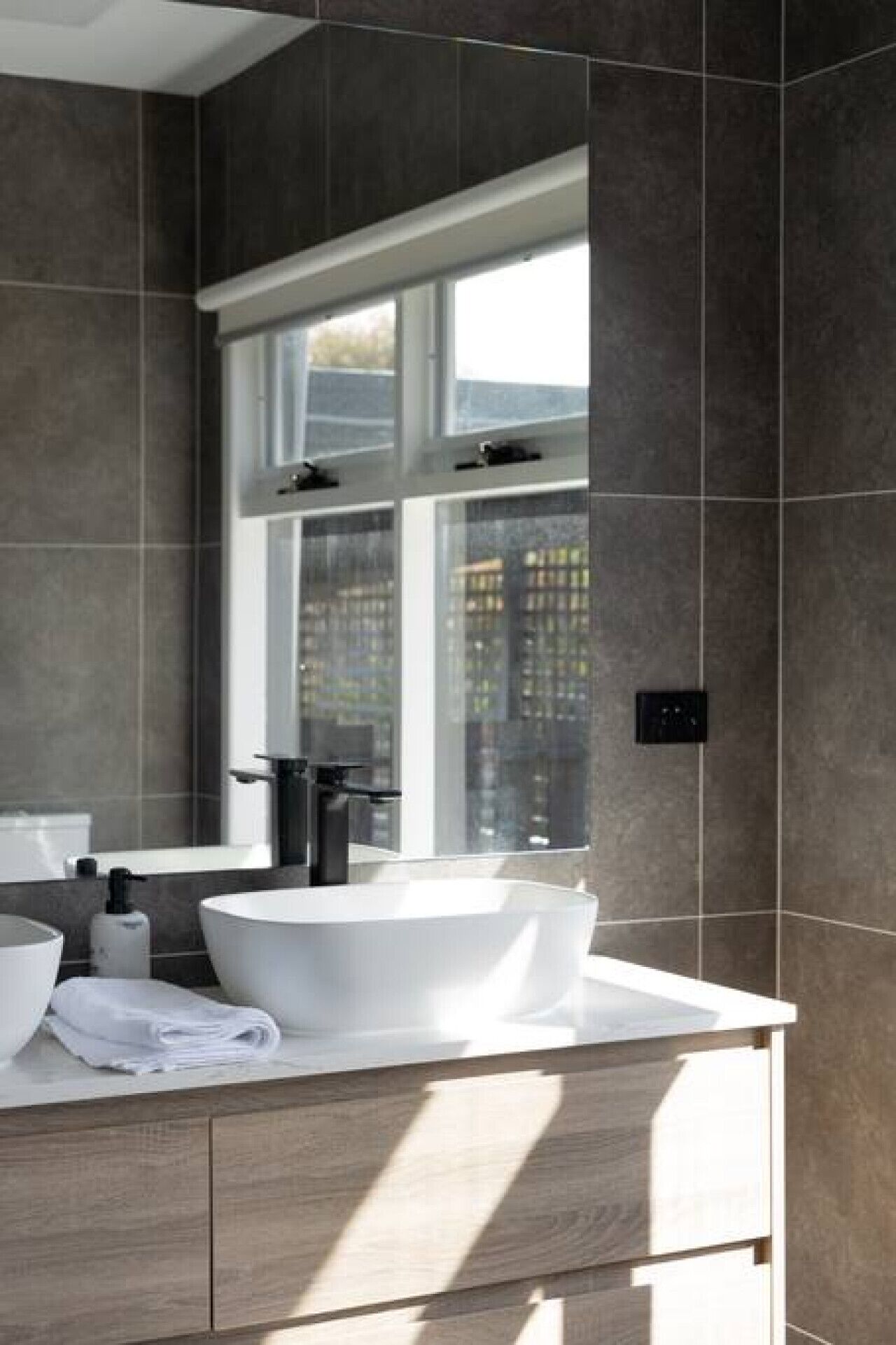 A modern bathroom with a large window, a white sink, and a wooden vanity.