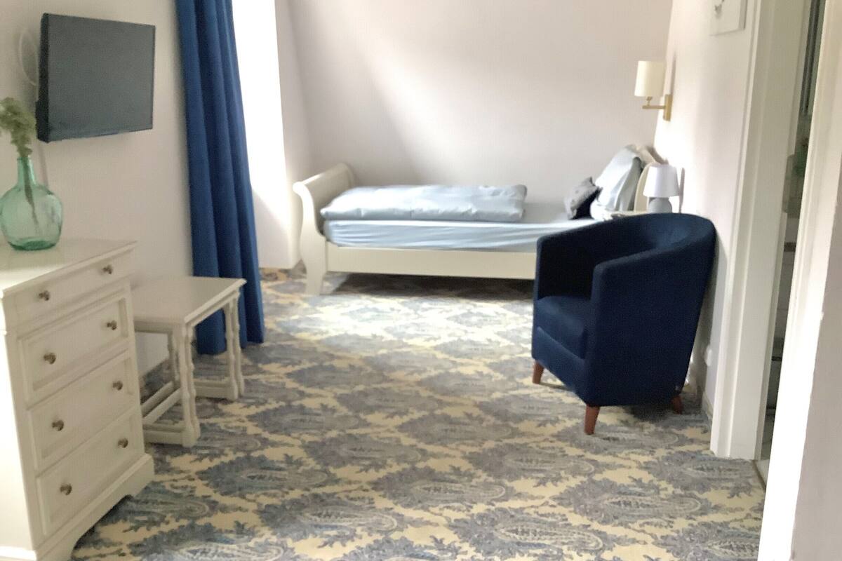 A bedroom with a bed, a dresser, a chair, and a patterned carpet.