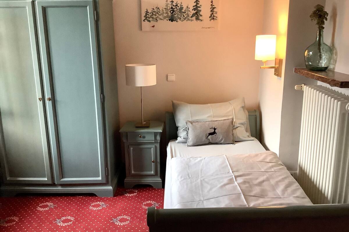 A bedroom with a bed, a nightstand, a lamp, a wardrobe, a radiator, and a wall art piece.