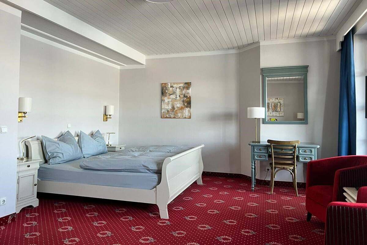 A hotel room with a bed, a desk, a chair, and a mirror.