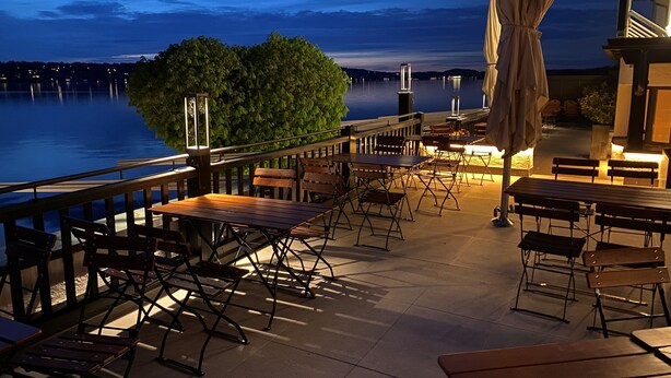 An outdoor patio with tables and chairs, overlooking a body of water. - Strandhotel Berg (Berg)
