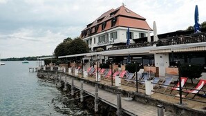 A waterfront building with a dock extending into the water, featuring outdoor seating and umbrellas. - Strandhotel Berg (Berg)