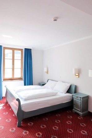 A hotel room with a bed, a nightstand, a lamp, and a window with curtains.