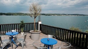 An outdoor deck with tables and chairs, overlooking a body of water. - Strandhotel Berg (Berg)